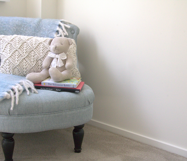 Teddy bear sitting in a newly renovated children's room on a blue chair with matching throw blanket and books