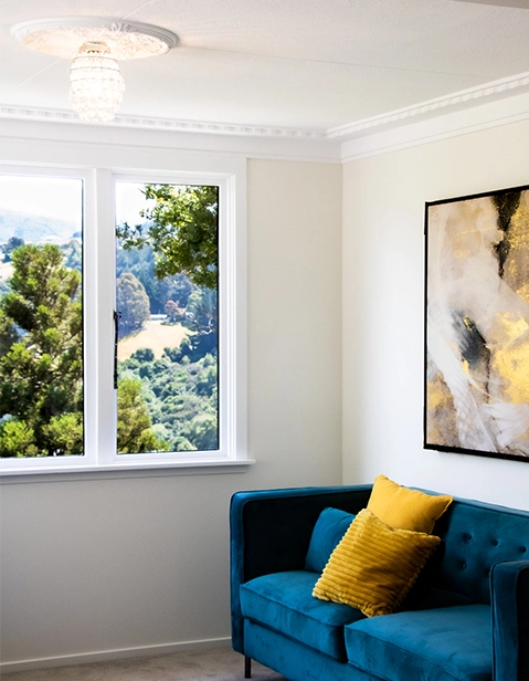 Interior of house, showing blue coach, under wall painting with view of trees in window